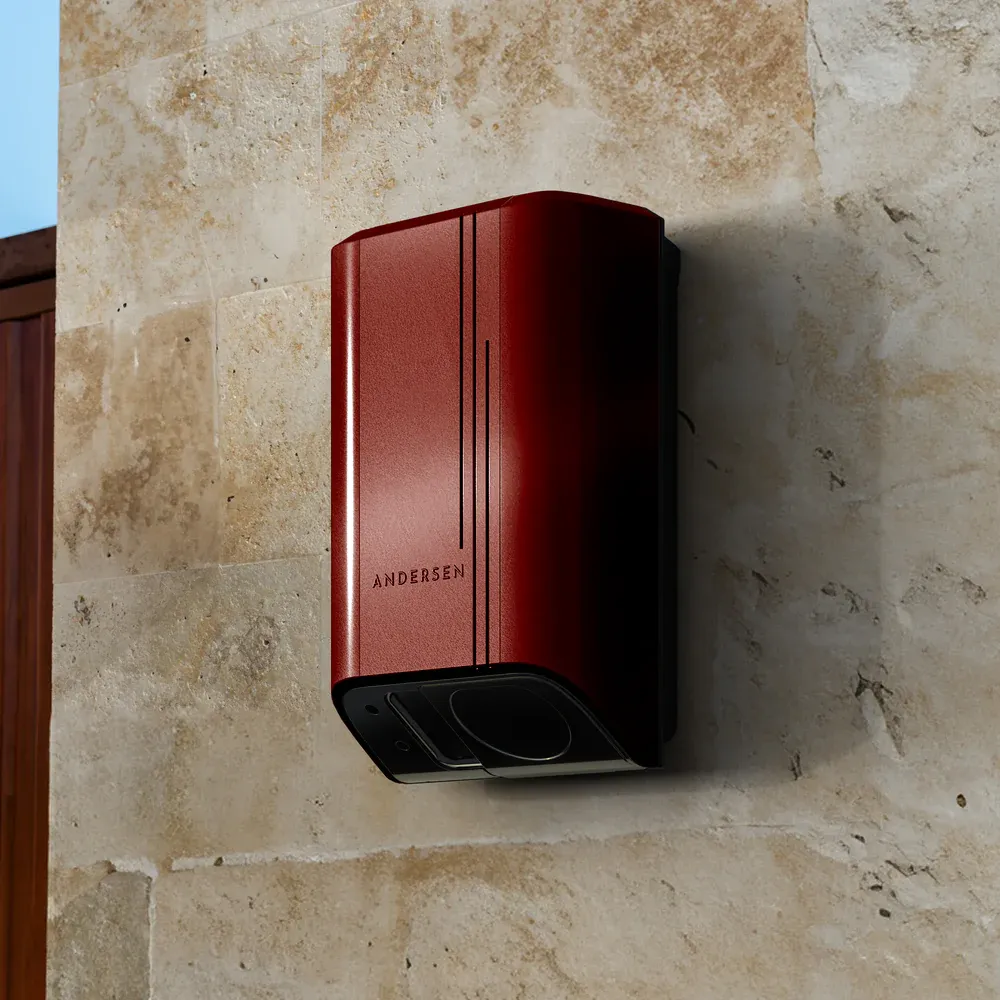 Andersen Quartz EV charger in red metal finish mounted on a natural stone wall, showcasing premium design and discreet cable concealment.